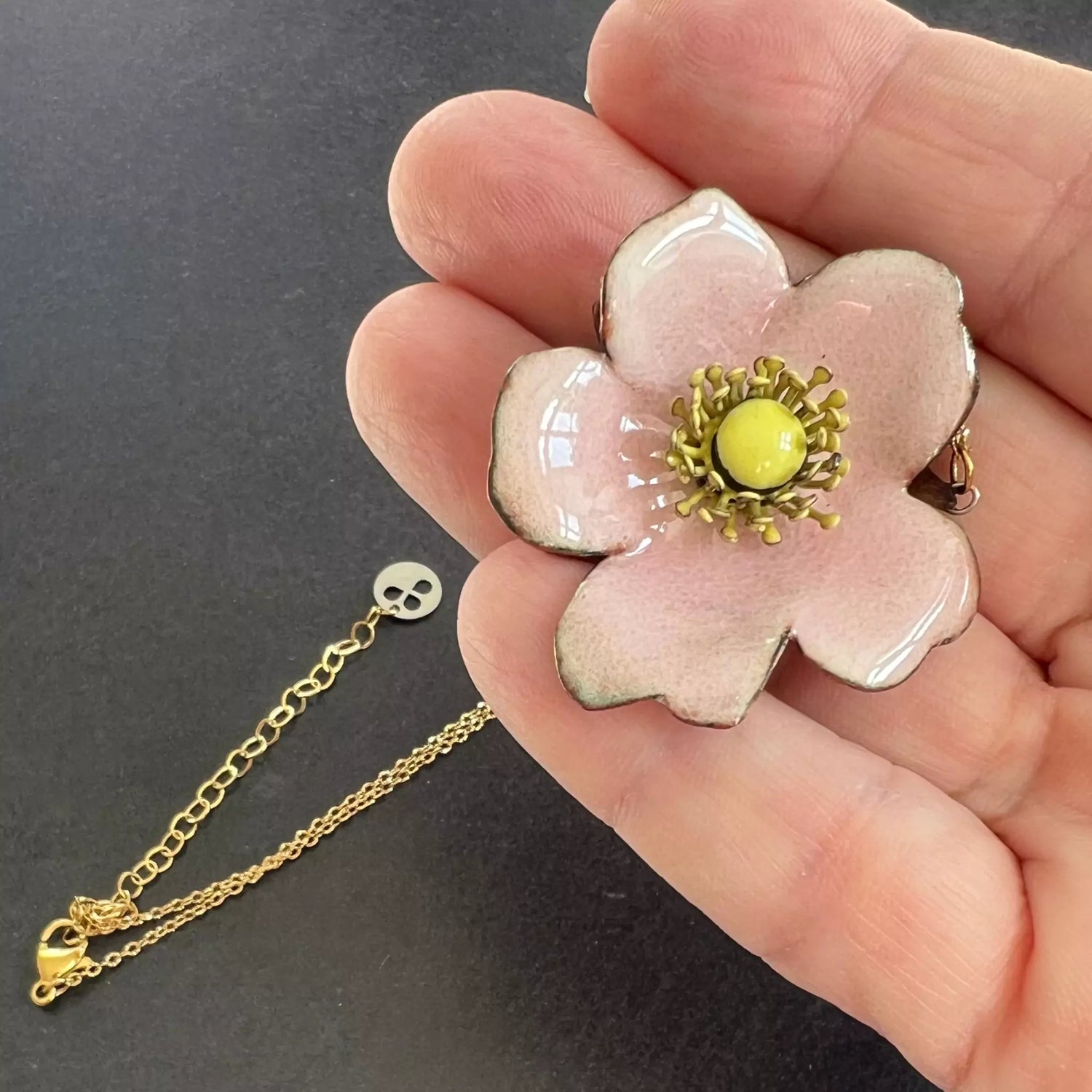 pendentif petite rose rose , son coeur et ses étamines émaillées jaune, et sa chaine en acier inoxydable teinte dorée. dans ma main
