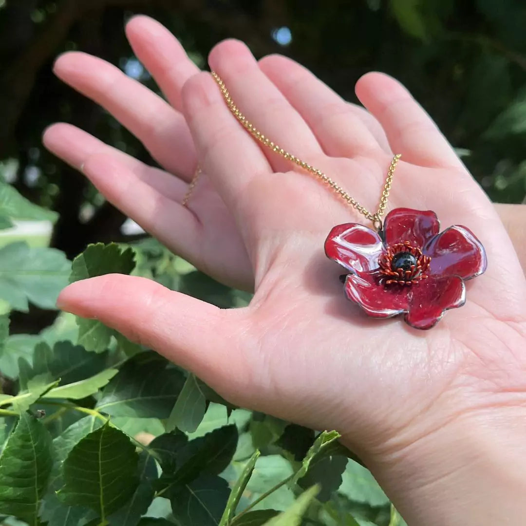 Ein handgefertigter Schmuck, ein emailliertes Schmuckstück, wie eine Blume in der Handfläche.