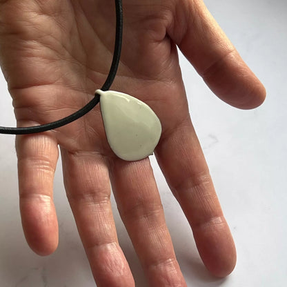 Creme Emaille Anhänger Rosenblütenblatt in der Hand mit schwarzem Lederband auf weißem Hintergrund